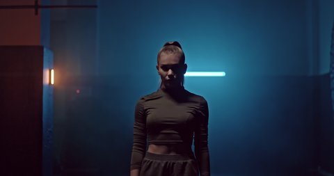Silhouette of a young female athlete in the dark hall of the fight club, smoke. Woman getting ready for fight club training, serious look. Beautiful female athlete before the fight in the gym. 4k