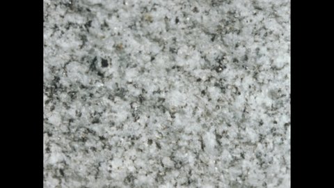 1950s: Hand rubs a speckled stone. Slabs of marble in a quarry. Rough cut surface of speckled marble.