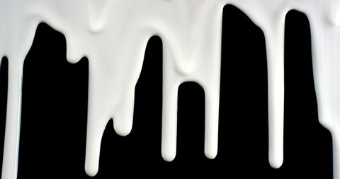 Trickles of spilled white liquid flow down the black background. Isolated white paint spilled onto black paper.