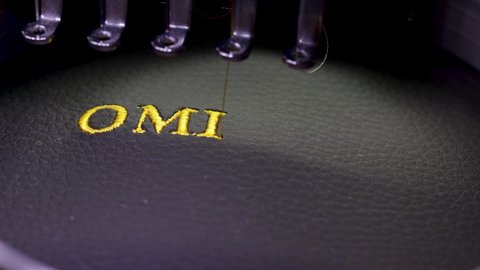 Machine embroidery with the inscription Omicron on black leather with yellow thread. Machine embroidery design, close up 4k video.
