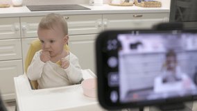 Parents record video on smartphone of kid in high chair at home, recording with mobile phone and ring light photo video of one-year-old baby boy with fruit. High quality 4k footage
