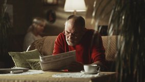 Senior woman hurrying to give tablet to elderly man finishing to read newspaper and falling down on sofa with severe chest pain - Powered by Shutterstock - Get 15% off with code: PIKWIZARD15