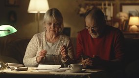 Elderly husband and wife analyzing utility bills and making calculations on smartphone while sitting near table in living room at home - Powered by Shutterstock - Get 15% off with code: PIKWIZARD15