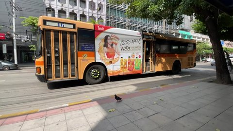 BANGKOK, THAILAND - Circa November, 2021: Air conditioning orange bus arriving at bus stop, masked woman gets off bus number 16 with advertisement sticker on the side and walks up to the footpath