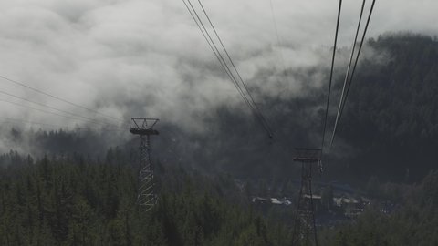North Vancouver, British Columbia, Canada. Aerial View of Gondola Tower over Evergreen Trees covered during winter season day. Grouse Mountain, Slow Motion