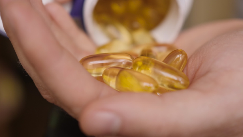 Man Pouring Fish Oil Capsules to Hand, Close up. Omega 3 Closeup. Omega 3 Gold Fish Oil Capsules. Natural Medicine, Sport, Healthy Lifestyle, Supplements, Dietary, Nutrition, Weight Loss, vitamin D.