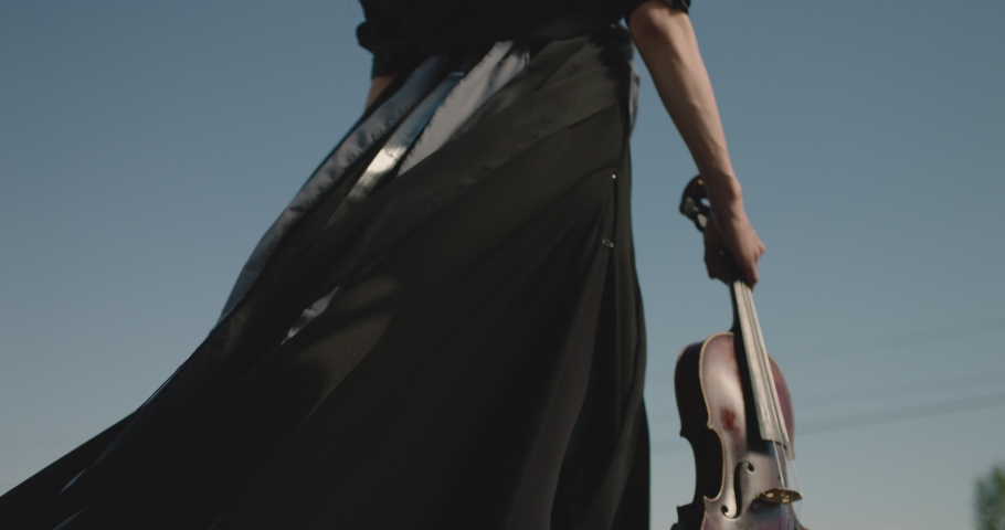 Back or side view of young musician woman holding wooden violin and walking . Rear view of black dressed woman walking in slow motion  . Classical musician theme or concept . Close up  Royalty-Free Stock Footage #1088238525