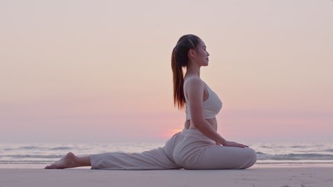 Young woman practicing yoga at the beach front for healthy mind and perfect body. At the beach and seaside make her feels relax spending holiday time in morning summer. Stretching her legs and arms.