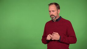 A middle-aged handsome Caucasian man hears a loud noise and covers his ears - green screen background