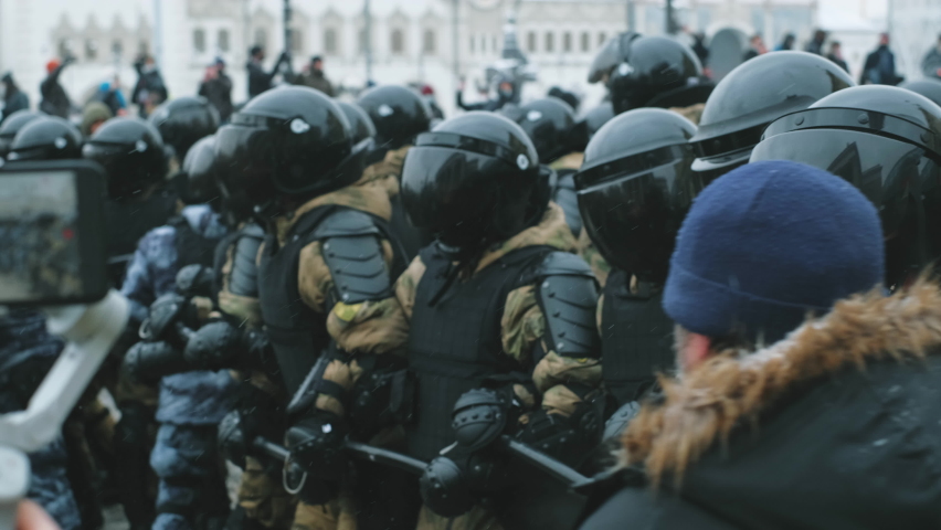 Riot police team with tinted visor on helmets. Policeman officers in rushing attack of protesting crowd on streets. Protesters on demonstration under police units offensive. Pushing line of police. Royalty-Free Stock Footage #1088241515