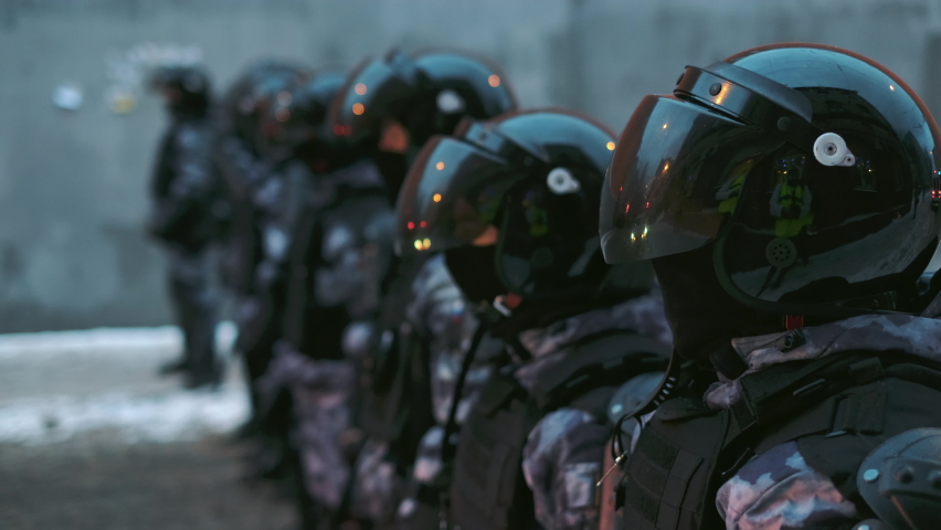Police officers from riot team unit block flashing city streets due to emergency. Men in armored uniform with protective helmets stand. Mirror like reflections of police strobe flash lights on visors. | Shutterstock HD Video #1088241559