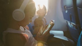 Kid schoolgirl in headphones watches cartoons in a phone on an airplane. little girl travels in an airplane, sitting in her seat, playing with a tablet computer, phone and headphones - Powered by Shutterstock - Get 15% off with code: PIKWIZARD15