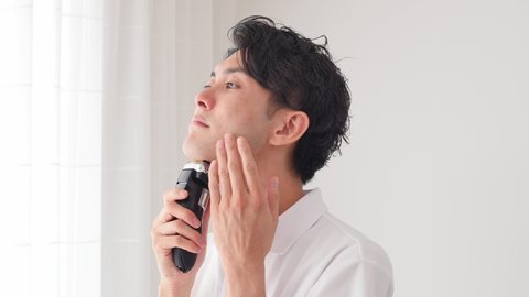Asian man shaving with electric shaver