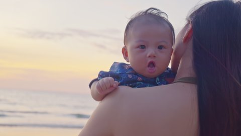 Asian mother holding her son at the sea sunrise beach front. Happy family vacation. Travel. Happy mom spending time with baby at the ocean vibes. Motherhood love and care for her child. 