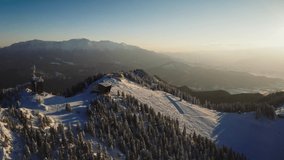 4k video. Aerial view of Poiana Brasov ski resort in Romania, next to Bucegi Mountains, win a beautiful winter landscape before sunset. Landmark of Romania.