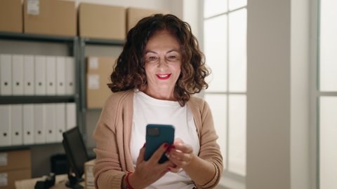 Middle age woman ecommerce business worker using smartphone at office