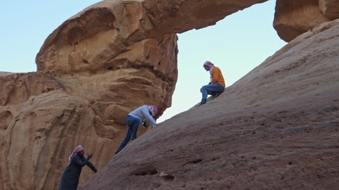 Wadi Rum desert, Valley of the Moon, Jordan FEBRUARY, 2, 2018 Tourists dangerous climb a steep rock face to reach a scenic natural rock bridge on background