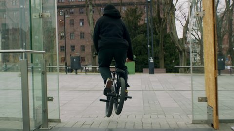 TRACKING Caucasian teenager kid performing tricks while riding his BMX bicycle in the city. Shot with 2x anamorphic lens