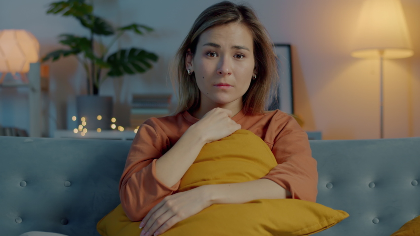 Portrait of beautiful young lady watching breaking news on TV and crying sitting on couch in dark room. Emotion and mass media concept. Royalty-Free Stock Footage #1088250205