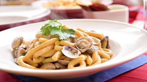 Vongole pasta in a white plate with hot steam. Fresh lunch in a traditional Italian restaurant thick pasta with clams and parsley, close-up. High quality FullHD footage