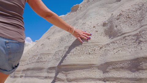 Slow motion close-up of a female sliding hand over a white rock formation showing strata layers on a sunny day in Milos, Greece