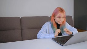 Cute Ukrainian girl with dyed rainbow hair typing text on laptop computer at home. Young adult female working online. Freelancer person doing distant work on modern notebook pc connected to internet