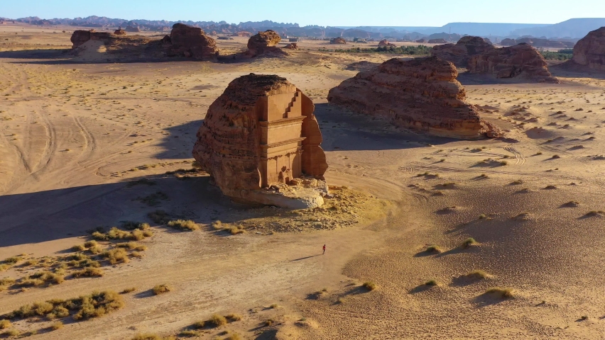 Aerial view overlooking a person running in front of the Hegra monument, in sunny Saudi Arabia - tilt, drone shot Royalty-Free Stock Footage #1088258601