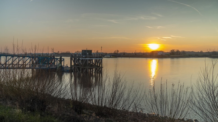 Sun setting down behind silhouette of small town. Pier in foreground with moving boats. Timelapse