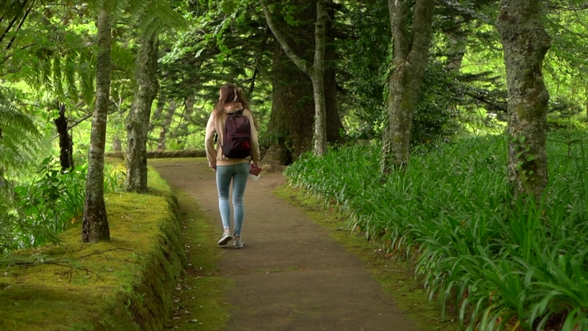 Woman walking in green park with backpack and map in hand slow motion following