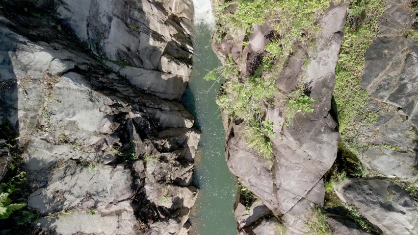 DRONE AERIAL SHOT IN WATERFALL SURROUNDED BY TREES AND ROCKS