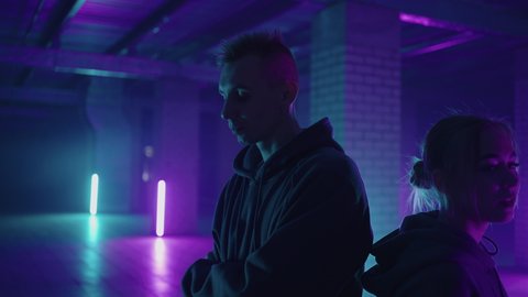 Two hip-hop dancers in neon light dance together in blue and purple colors. Women enjoying hip hop moves in dark studio with smoke and lighting.
