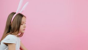 Side view video of a little girl with bunny ears on head receiving tulips from somebody on pink background and copy space.