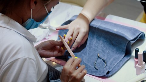 Beautician removes old varnish with a manicure file for nails. Removal of old gel. A woman manicurist removes shellac gel from a client's nails with a manual pedicure file.
