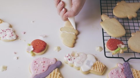 Woman squeezing icing cover on cookies from a pastry bag. Decorating sugar cookies in lolly ice cream shape with sugar glaze. Camera zoom in. Summer concept. 4K UHD
