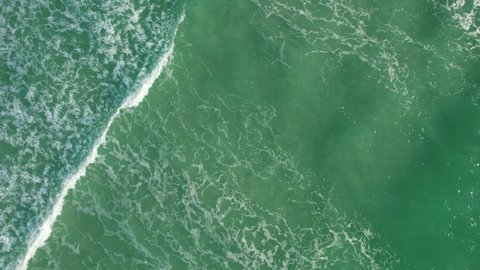 Aerial shot of the Atlantic ocean water in a tropical city of Miami. Waves moving to the beach line.  Background drone shot of the blue and green water. 