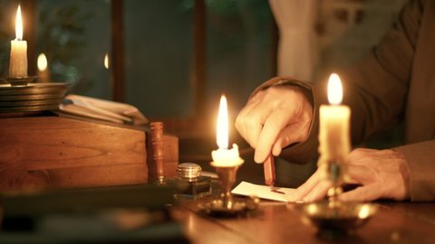 A scene from the 18th century of a man melting sealing wax by candle flame to use to seal a letter he has written.