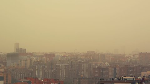 MADRID, SPAIN. March 15 2022. Pan shot of a panoramic view of Madrid’s skyline with Torrespana communications tower, also known as Piruli, partially covered by an orange dust storm from Sahara desert