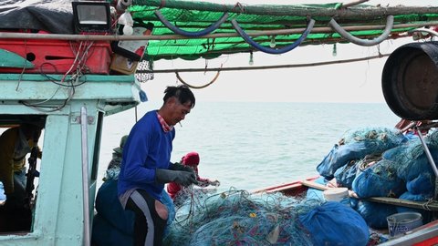 Pattaya , Chonburi , Thailand - 12 03 2021: Mending the net while smoking then smiles at the camera as the boat moves with the waves, Pattaya Fishing Dock, Chonburi, Thailand.