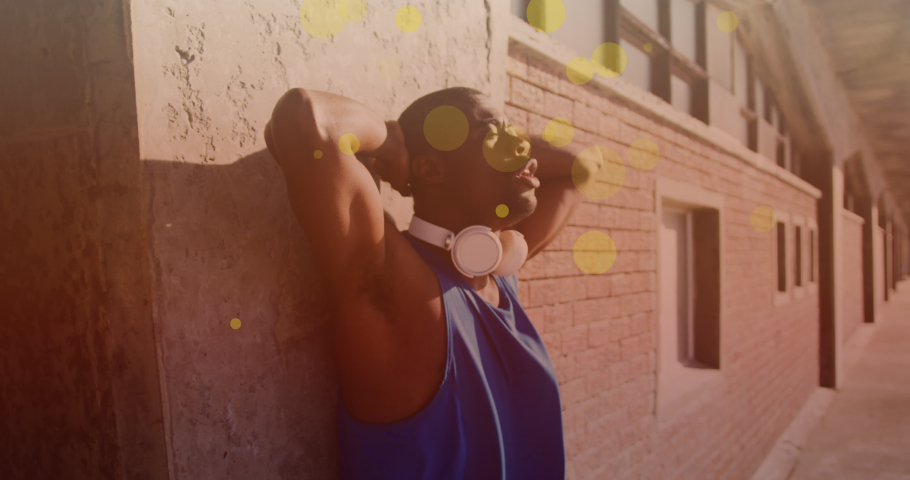 Yellow spots floating against tired african american fit man taking a break from running. sports, fitness and technology concept