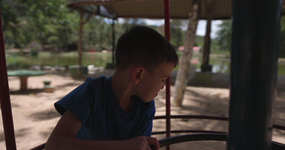 Happy young boy spins around merry go round in park - medium shot of smiling face Royalty-Free Stock Footage #1088268917