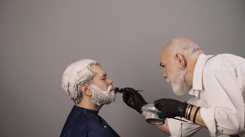 Professional hairdresser dying hair of bearded man in barber shop. Professional hairdresser drying hair in studio.