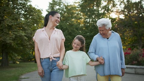 Small girl with mother and grandmother in a park, walking in park.