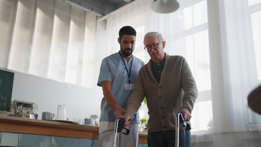 Caregiver helping senior man to walk with walker indoors in retirement nursing hme. | Shutterstock HD Video #1088271647