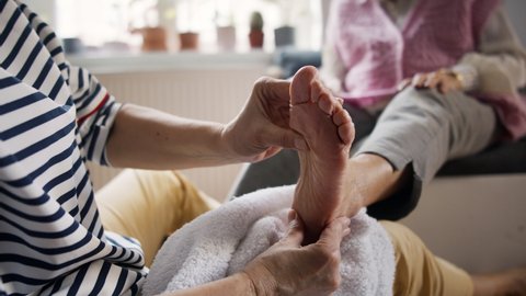 Close-up of senior woman receiving a pedicure from healthcare worker at home, beauty spa concept.