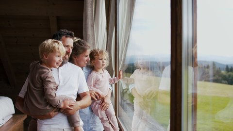Happy young family in pajamas with small children looking at view from window on holiday.