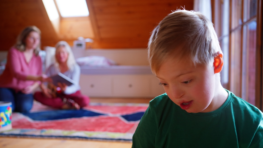 Little boy with Down syndrome sitting on bed at home.
