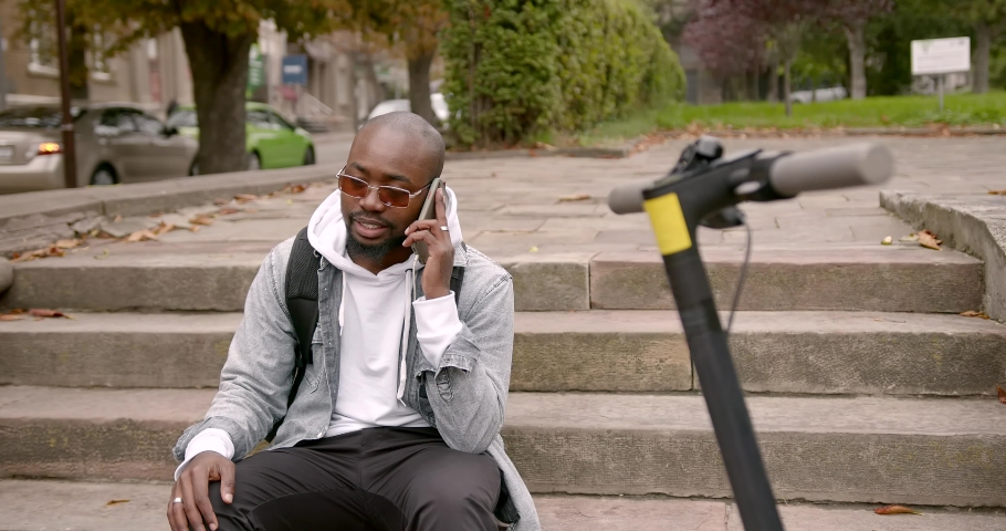 Black man sitting on the stairs near an electric scooter