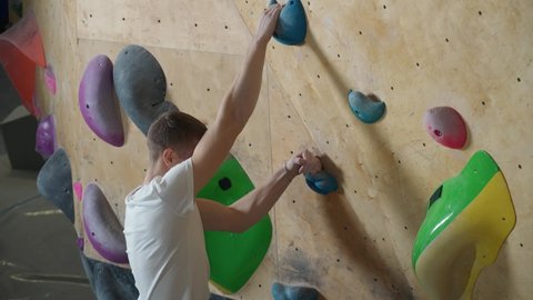 Young man climber training on a climbing wall, practicing rock-climbing, view from above.