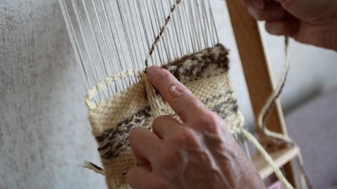 Artisan uses a tapestry beater to push weft threads down. Making mini tapestry piece with hand loom and weft beater