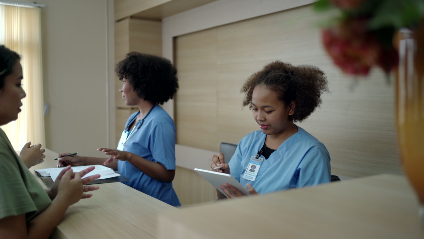 People making an appointment with medical staffs at reception desk in hospital. Medical staff and nurse - receptionist talking to patient in front of the reception counter in hospital. Royalty-Free Stock Footage #1088274641